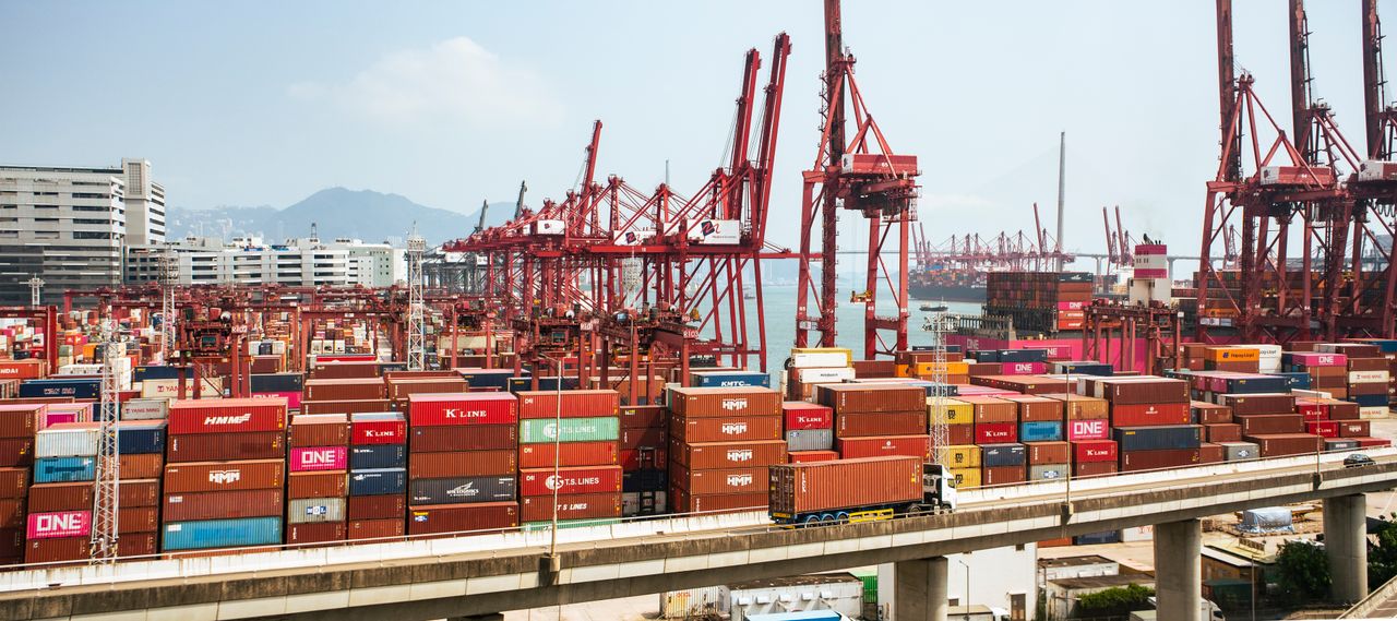 gallery-06 A bustling scene of cargo containers and cranes at a Hong Kong port, showcasing global trade.