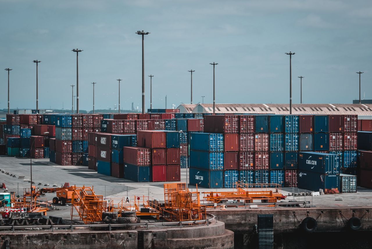 services-03 Colorful cargo containers stacked at a busy industrial port, showcasing global trade.