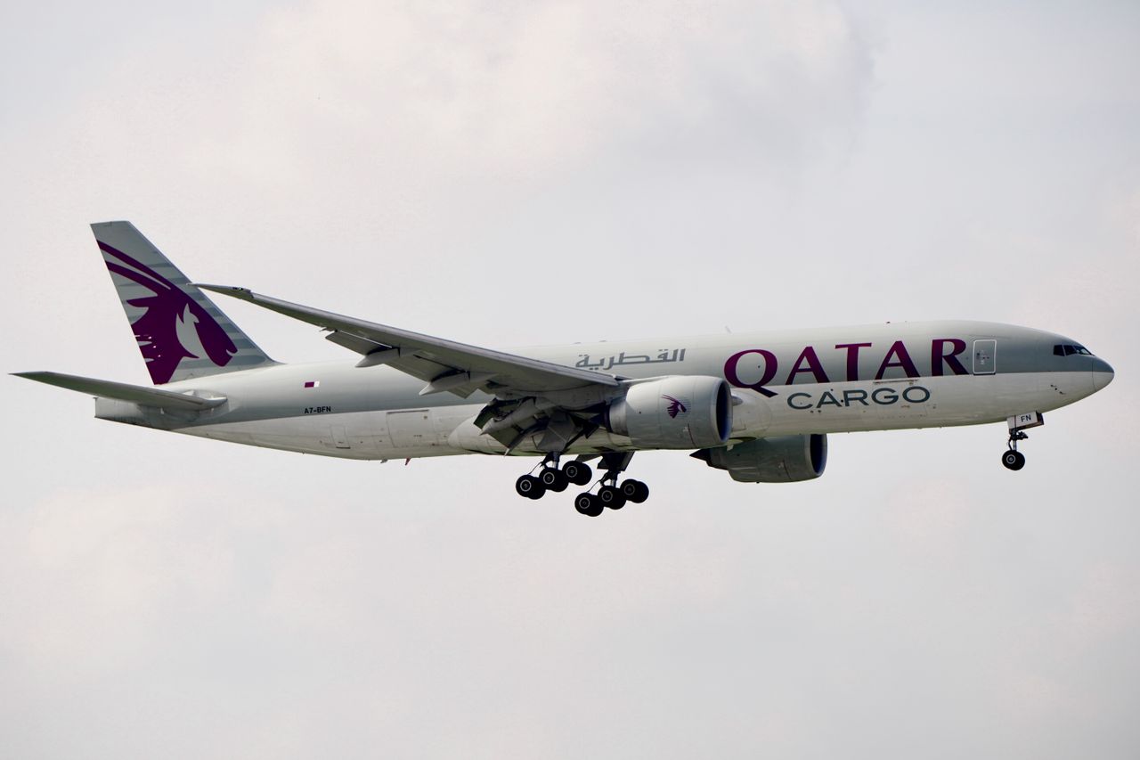 contact Qatar Airways cargo plane flying through the sky with landing gear down.