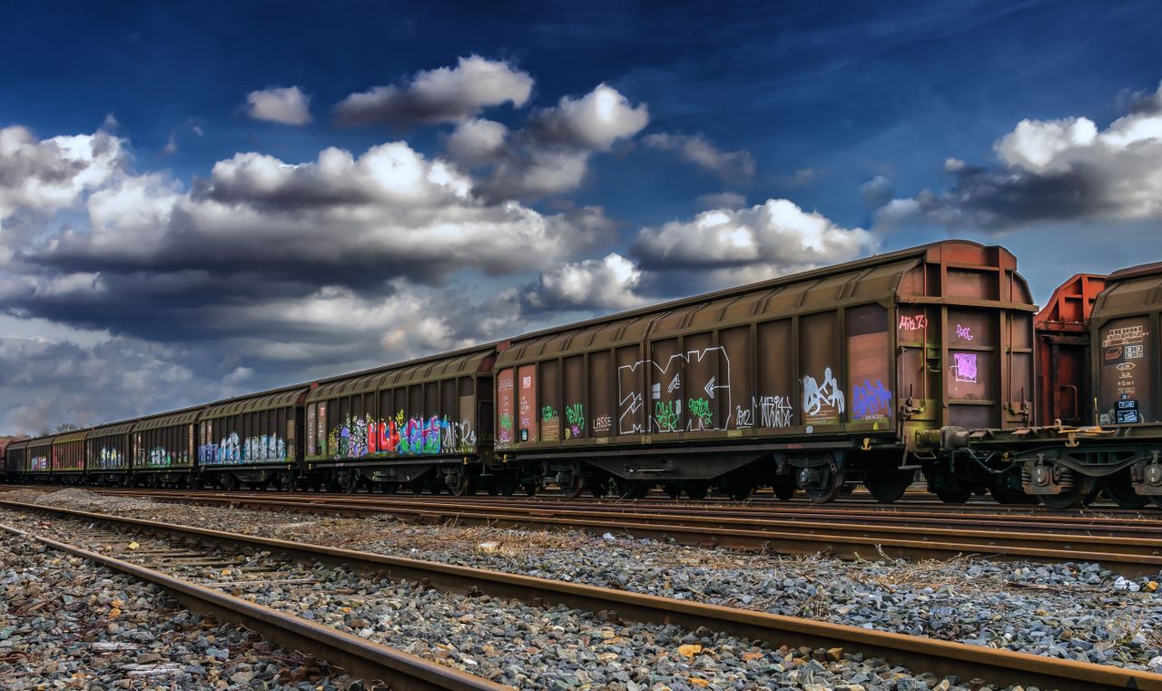 Freight train in a railway yard with colorful graffiti under a cloudy sky.